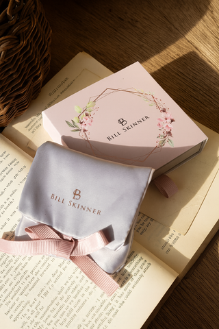 Bill Skinner product packaging with a pink box and gray pouch on an open book.