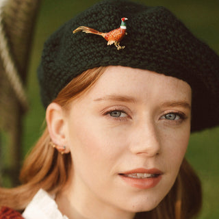 Woman wearing a black knit hat with a decorative pheasant brooch against a blurred natural background