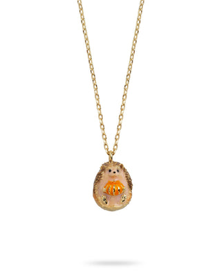 A gold chain necklace with a small, whimsical pendant shaped like a hedgehog holding a glowing orange pumpkin, set against a plain white background.
