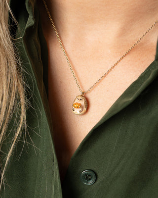 A gold chain necklace with a small, detailed pendant featuring a hedgehog character, shown worn on a model's neck over an olive green shirt.